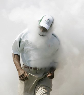 Miami head coach Randy Shannon is enveloped in a cloud of smoke from a fire extinguisher as he runs out onto the field with the team before a football...
