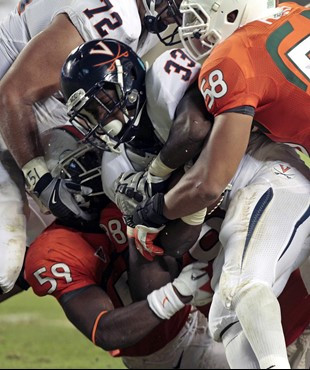 Miami's James Gaines (59) and Jordan Futch (58) bring down Virginia's Perry Jones (33) in the first half of an NCAA college football game in Miami,...